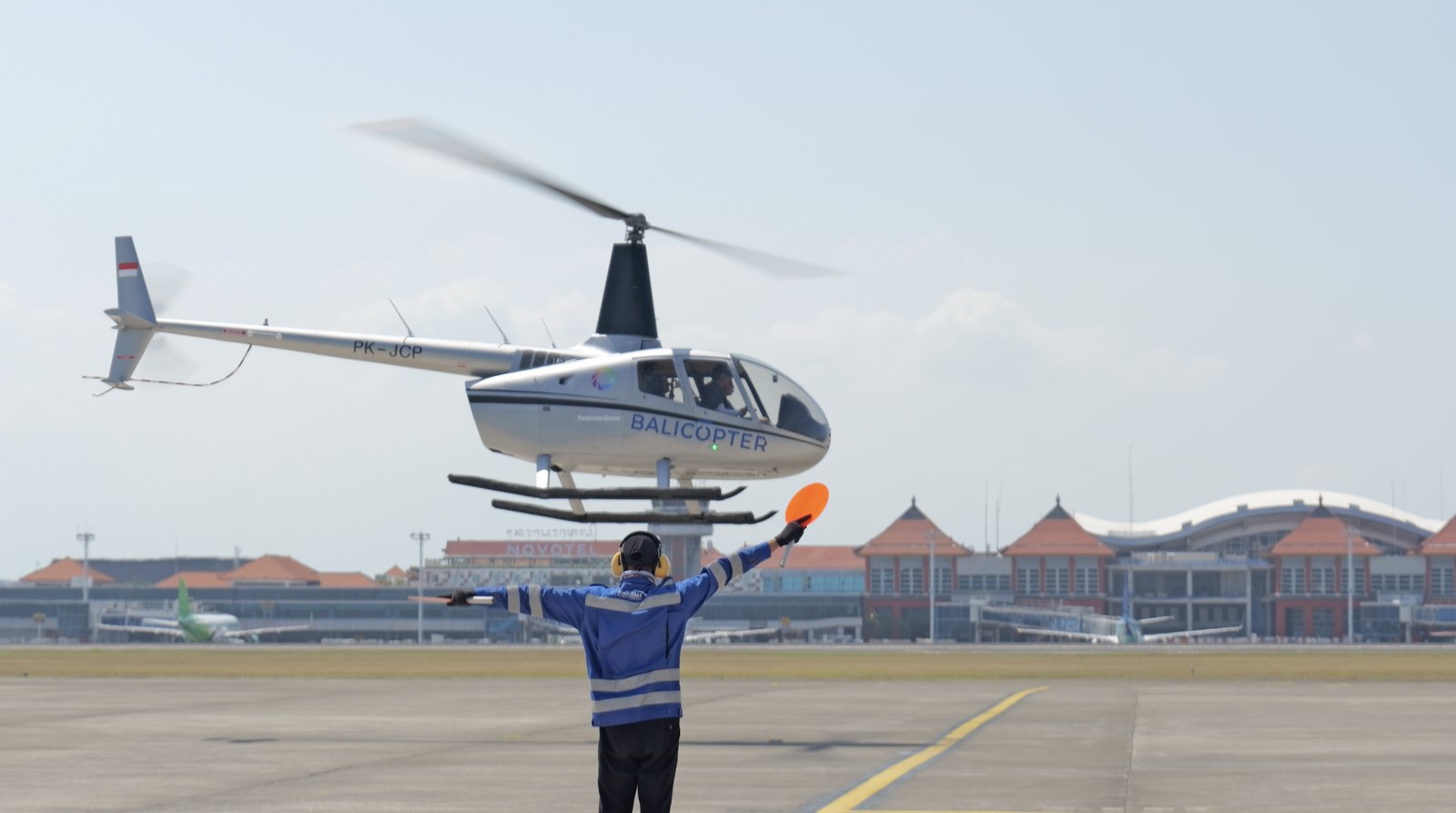 A helicopter hovering at Ngurah Rai International Airport, guided in by a marshaller